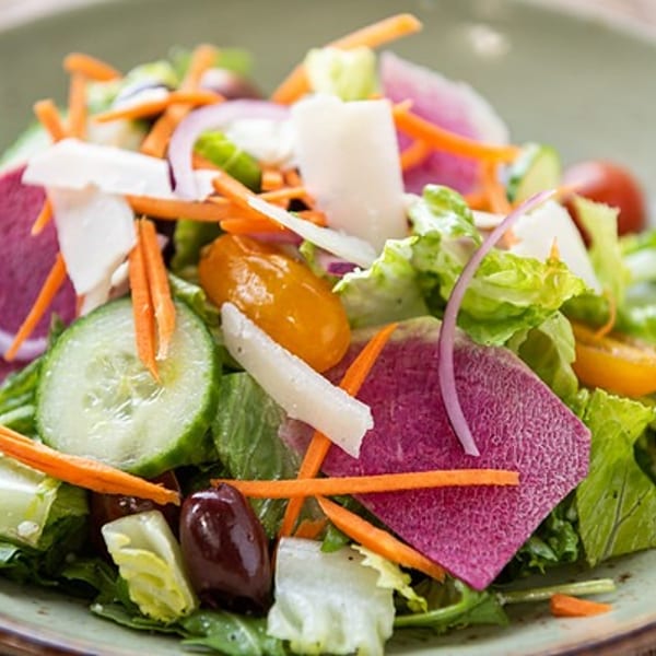 Close-up of a colorful garden salad with lettuce, cucumbers, carrots, radishes, and olives.