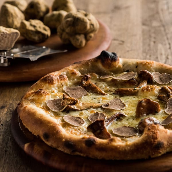 Truffle pizza with shaved truffles and whole truffles on a wooden board.